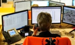 Emergency dispatcher on phone in front of multiple computer screens displaying maps and data.